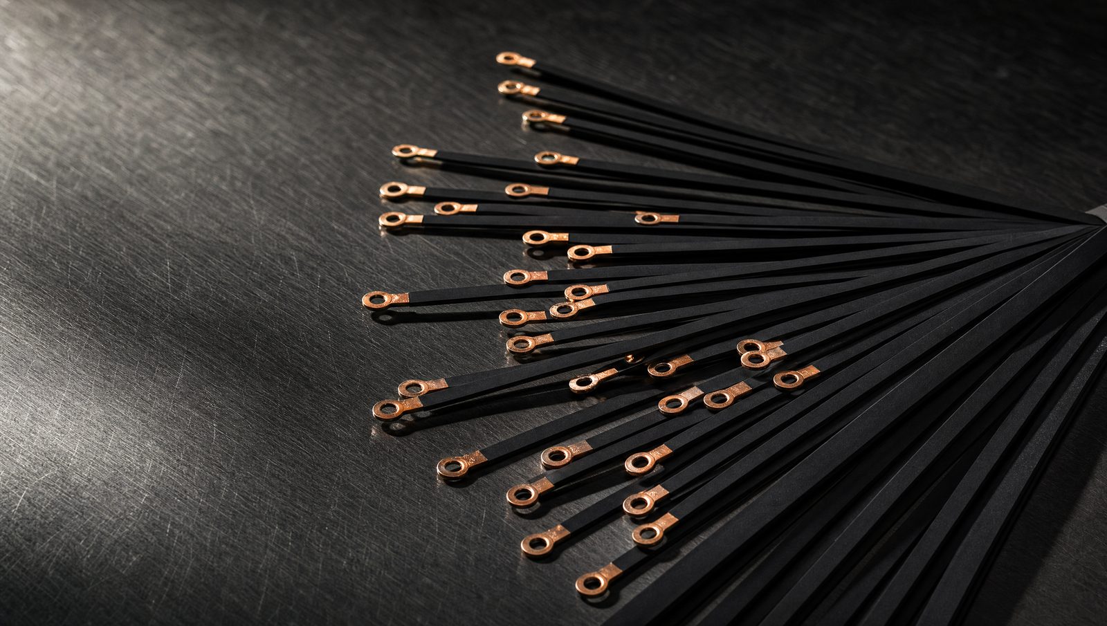 Flat heat seal elements with copper ring terminal ends, fanned out on a dark steel surface.