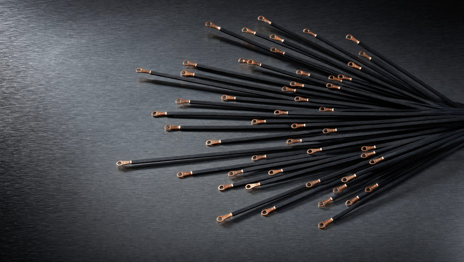 A fan of flat impulse heat seal elements, thin black PTFE coated steel ribbon with bright copper ring terminal ends.